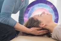 Somatic therapy in psychedelic therapy. The image depicts a serene scene of a woman lying on her back, receiving a gentle craniosacral therapy or healing touch. A person, wearing a long-sleeved blue-gray shirt, cradles the woman’s head with both hands, providing a sense of care and support. Behind the woman's head is a circular, dreamy, watercolor-like background composed of concentric rings in shades of purple, blue, and pink, adding a spiritual and calming atmosphere. The overall color palette is soft and soothing, with the focus on the gentle touch and the ethereal, abstract backdrop.