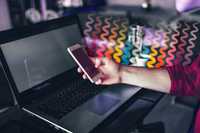 Alternative ADHD Treatment. Image of a laptop from an angled view with a person's hand hovering above it. The hand is holding a smartphone. Flowing from the phone, hand and forearm are squiggly lines in different colours.