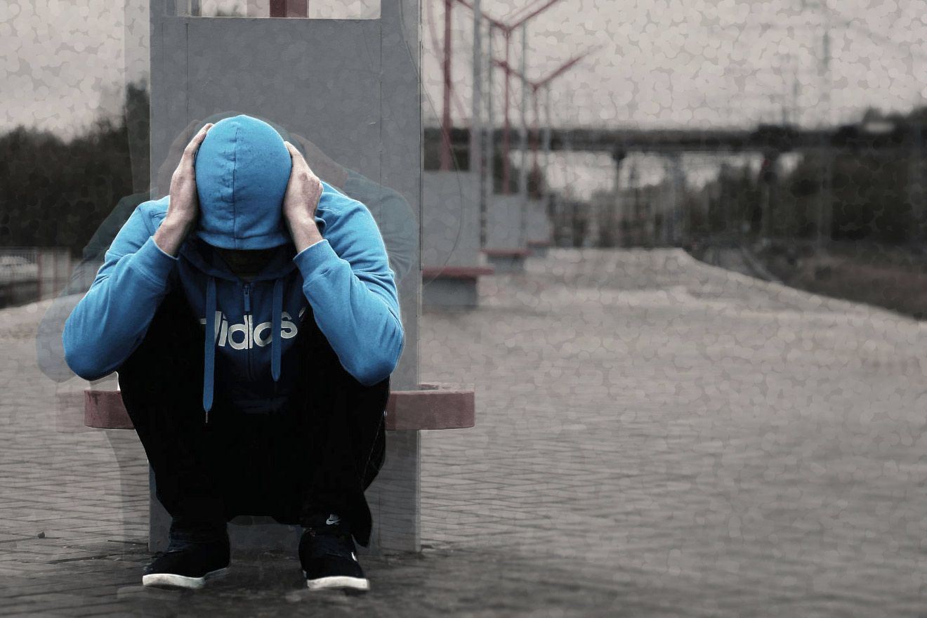 A man sits on the corner with his hands on his ears