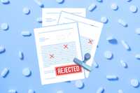 FDA's decision. A top-down view of documents with a large red 'REJECTED' stamp on a blue background with pills scattered around, scientific document, rejection letter, failed medicine