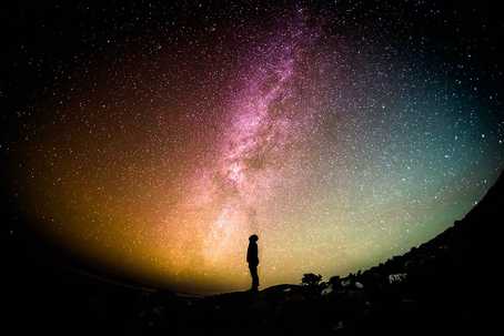 silouetted person looking up at a rainbow Milky Way, by Greg Rakozy