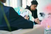 Mental Health Nursing. A person facing away from the camera holding a clipboard, with psychedelic sparkly patterns emanating from it. In front of them is another person, also seated and leaning forward with their arms on their lap.