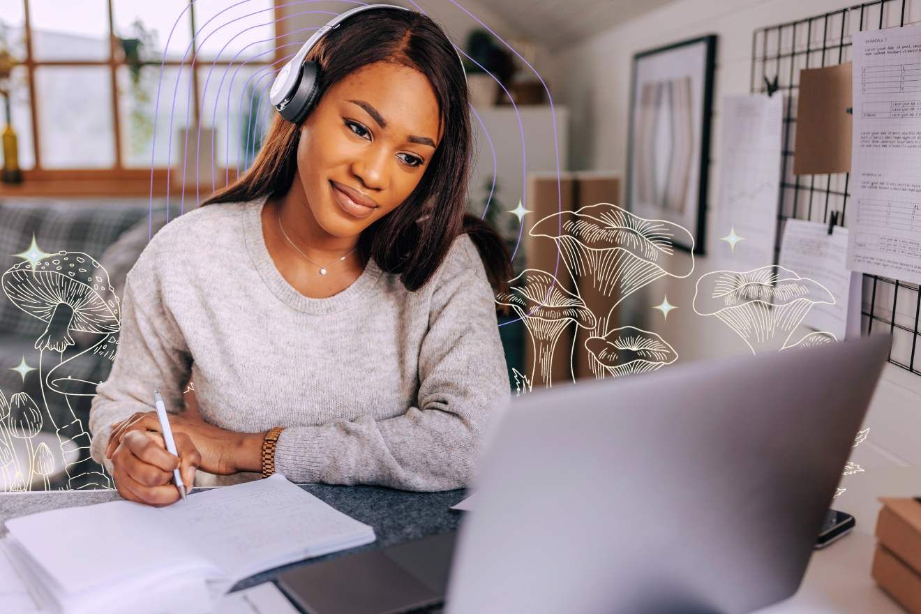 Psychedelic Preparation. Image of a female-presenting person with dark brown hear sitting at a desk, with a pen in their hand and a notepad before them. There is also a laptop in front of them, The room behind them looks like it could be their home. There are graphic lie drawings of psilocybin on either side of them, as well as some repeated lines arching around them, as well as some stars dotted around the image.