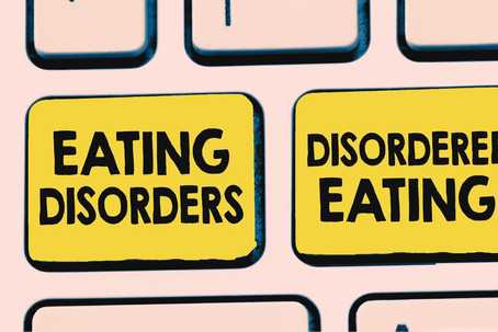 How Disordered Eating Isn’t The Same as an Eating Disorder. Image is of a close up of some keyboard keys. The background is peach, with a couple of black outlines of the keys. Two of the keys are a deep, dusty yellow. The one on the left reads "Eating Disorders" and the one on the right reads "Disordered Eating".